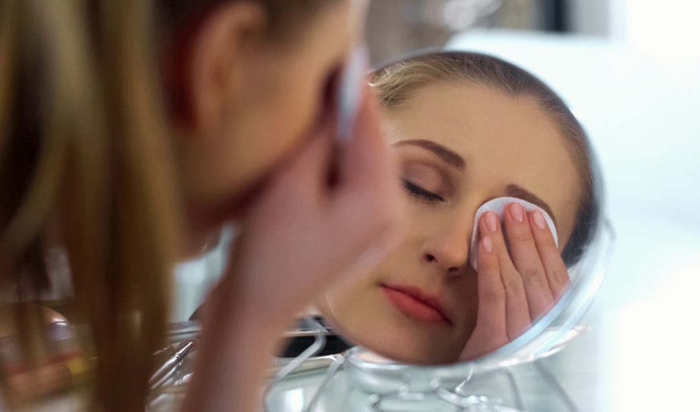A close-up of a woman gently removing her eye makeup with a cotton pad, demonstrating proper skincare application.
