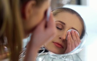 A close-up of a woman gently removing her eye makeup with a cotton pad, demonstrating proper skincare application.