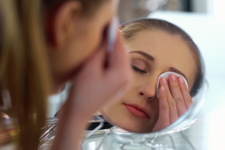 A close-up of a woman gently removing her eye makeup with a cotton pad, demonstrating proper skincare application.