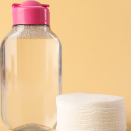 A minimalist bottle of micellar water placed next to a stack of clean cotton pads